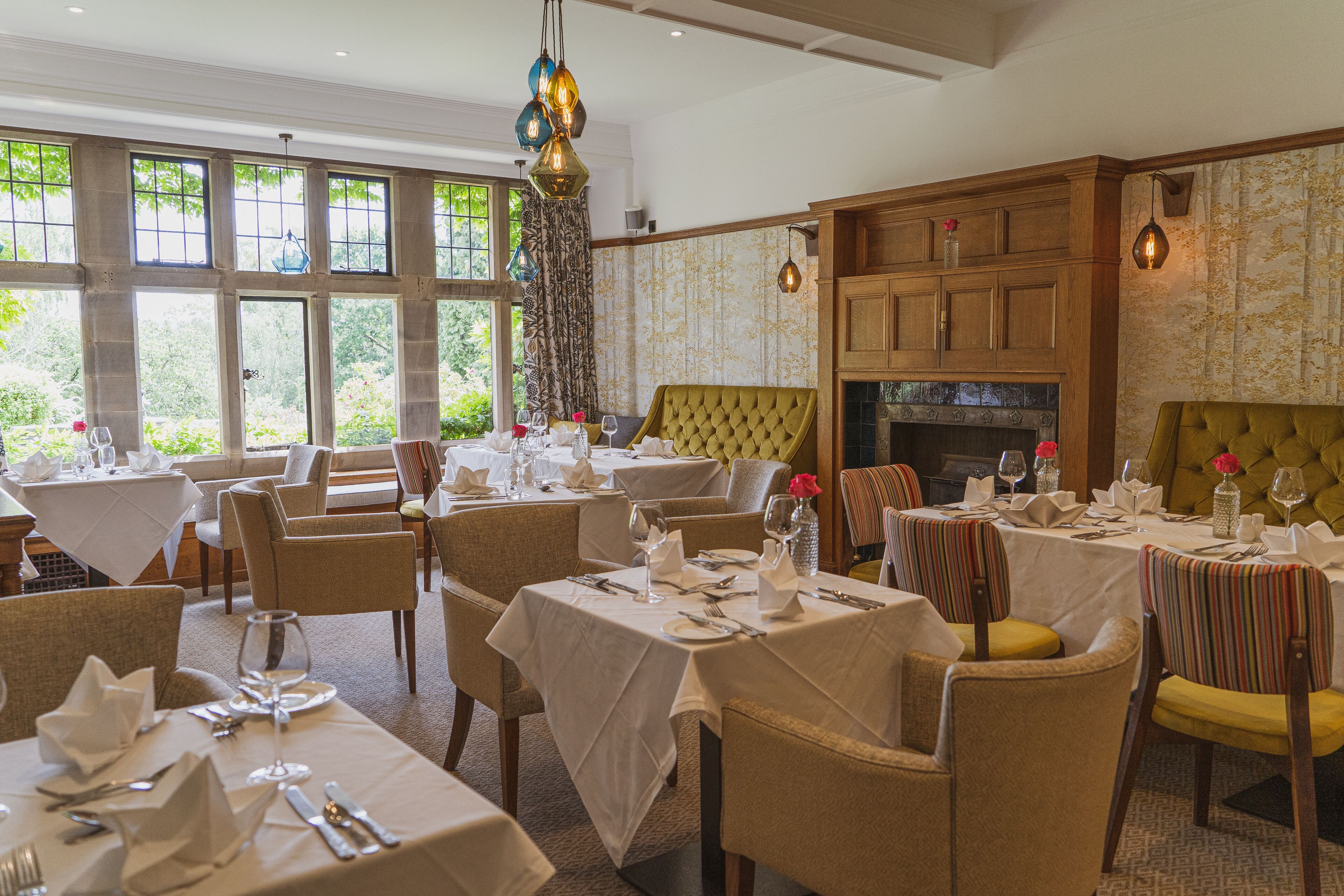 A dining area with multiple tables set for dining, chairs, and a fireplace.