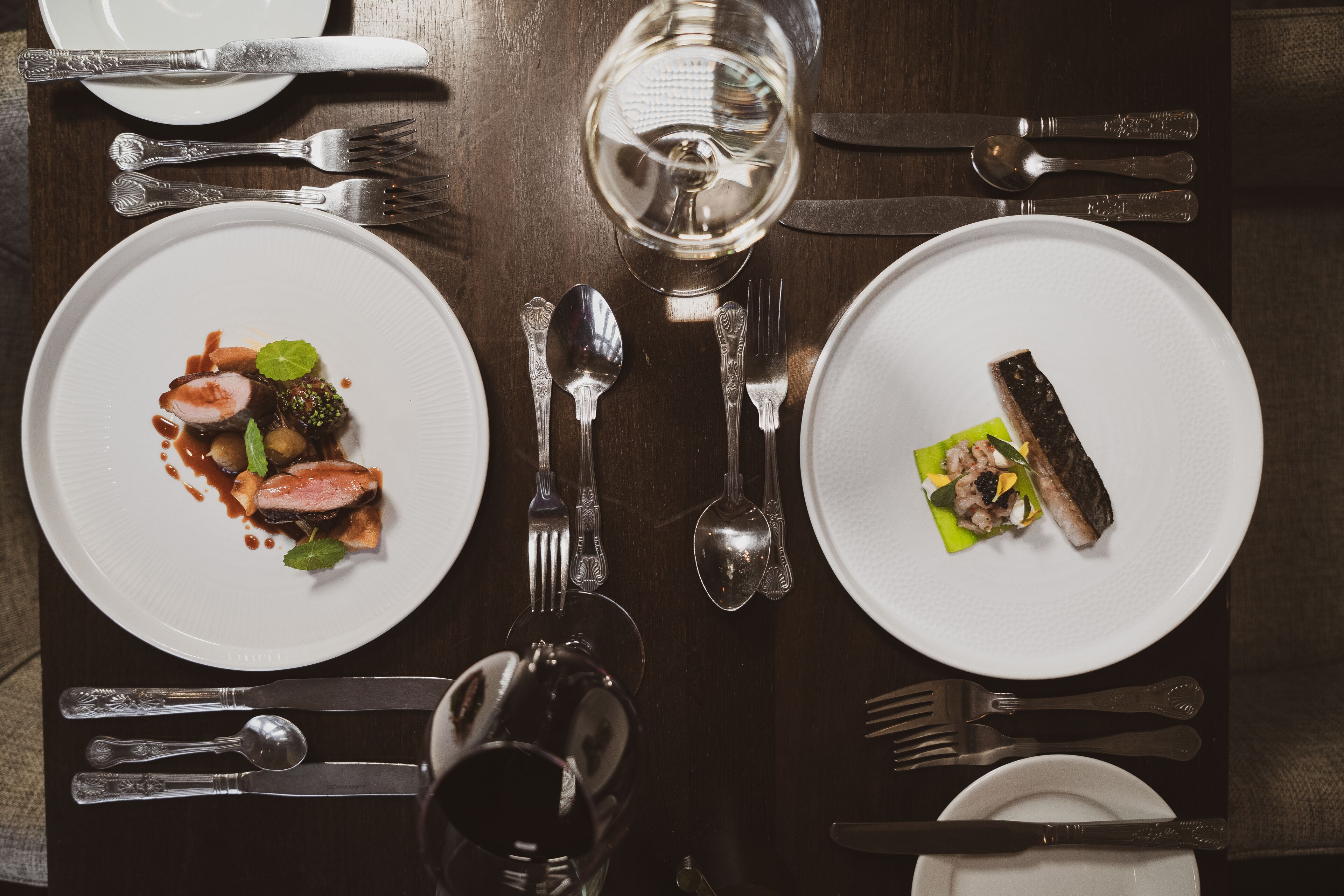 A dining table set with plates of food, cutlery, and a glass of water.