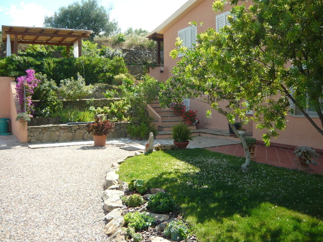 A garden with a stone wall, a pergola, and a variety of potted plants.