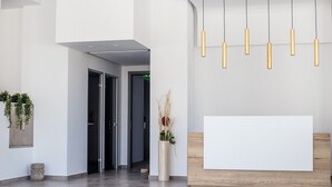 A modern reception area with a wooden reception desk, a large blank sign, and a tall vase with dried plants. - Moscha Hotel (Rhodes)