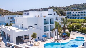 A modern hotel with a pool area, multiple balconies, and a view of the surrounding landscape. - Moscha Hotel (Rhodes)