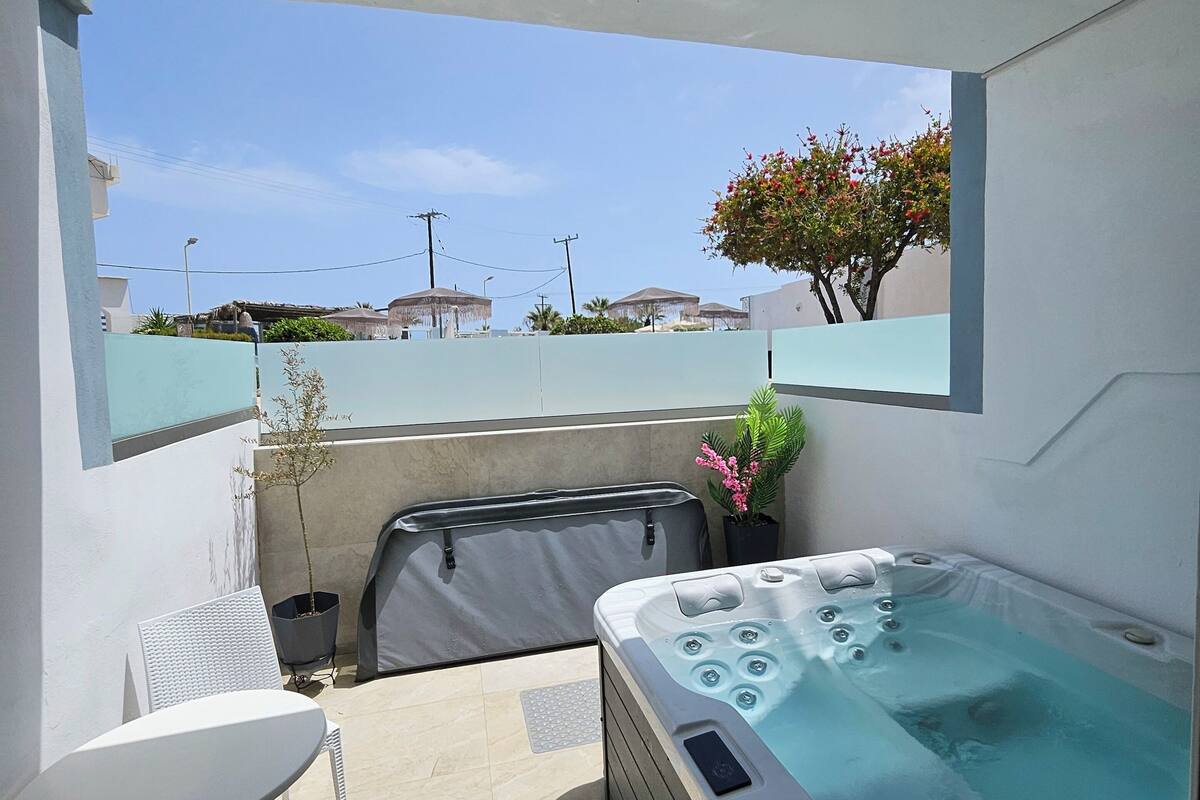Un balcón con jacuzzi, una mesa y sillas, con vistas a una zona residencial con casas y un cielo despejado.
