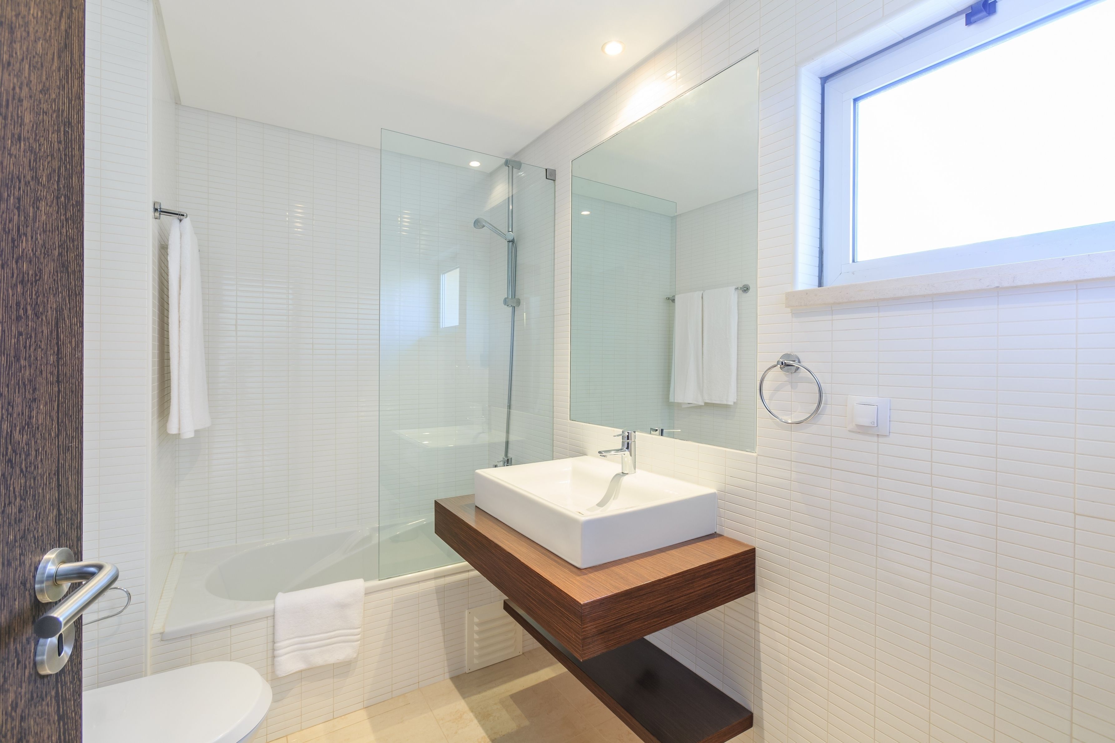 A modern bathroom with a glass-enclosed shower, a freestanding bathtub, and a wooden vanity with a white sink.