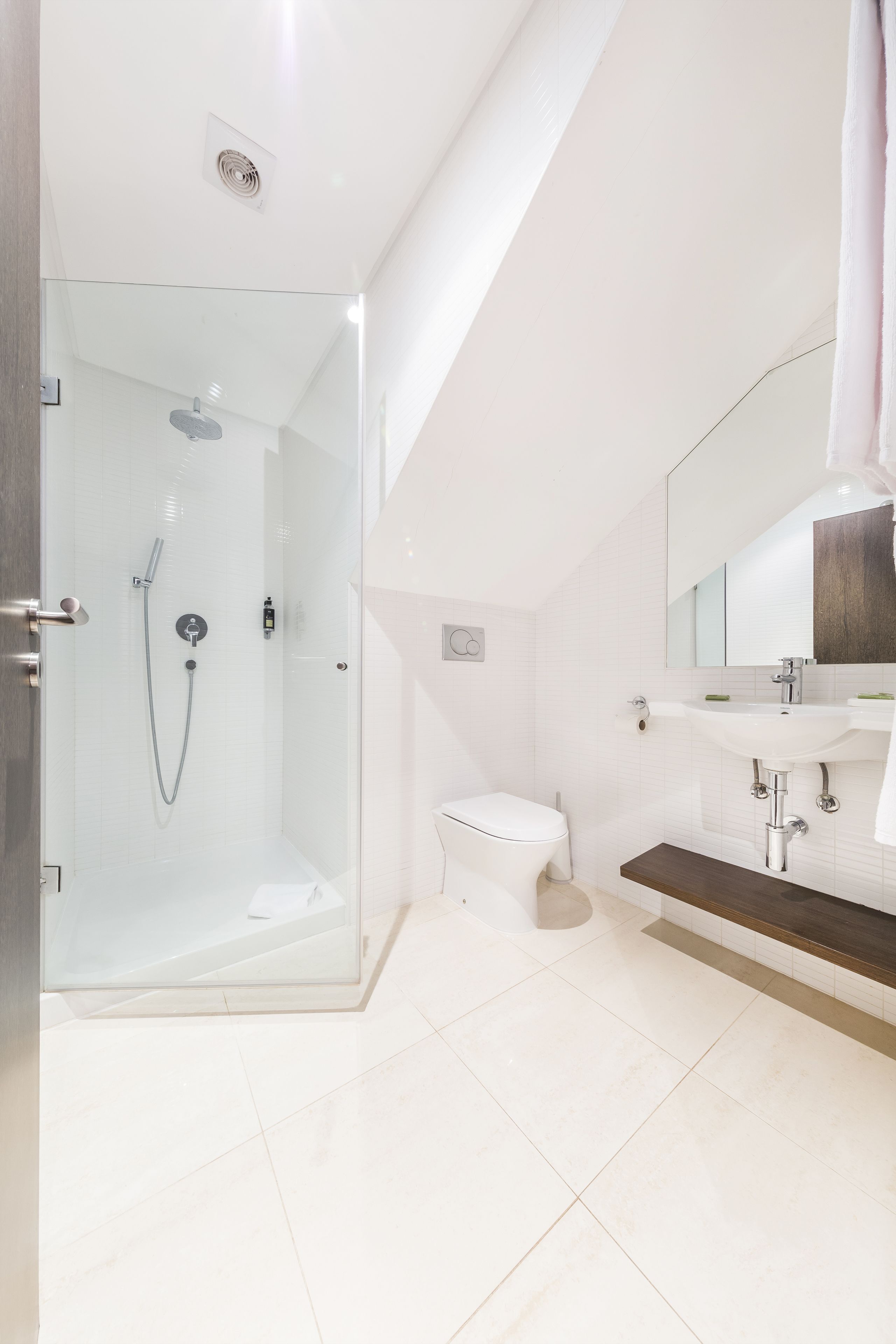 Un baño moderno con ducha separada por vidrio, inodoro blanco y lavamanos con encimera de madera.