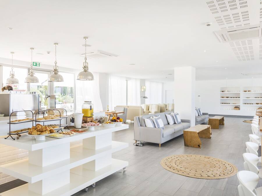 Un área de estar luminosa y moderna con una mesa de buffet, asientos y un amplio ventanal que proporciona luz natural.