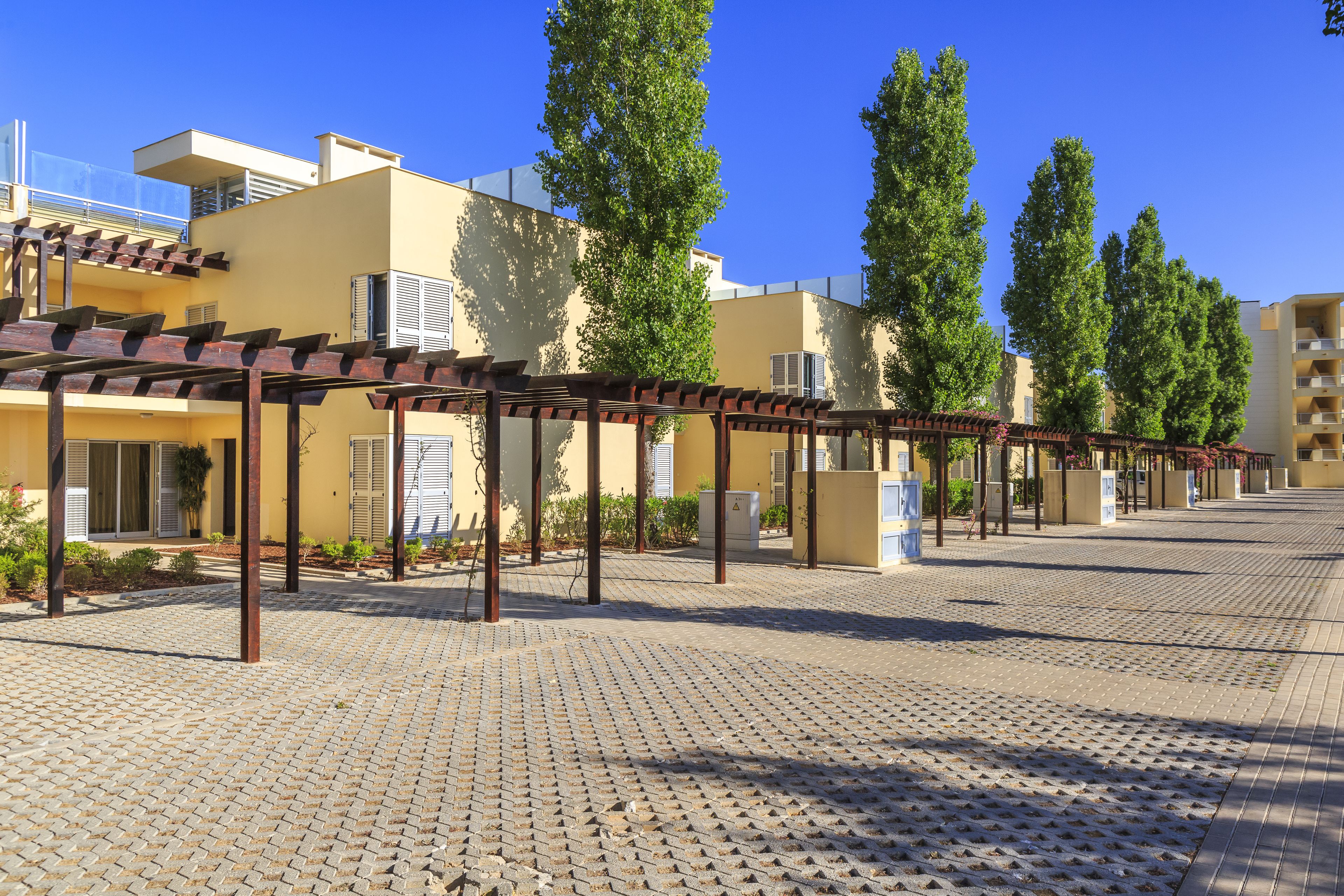 Un patio con pérgola, pavimento de baldosas y edificios con balcones.