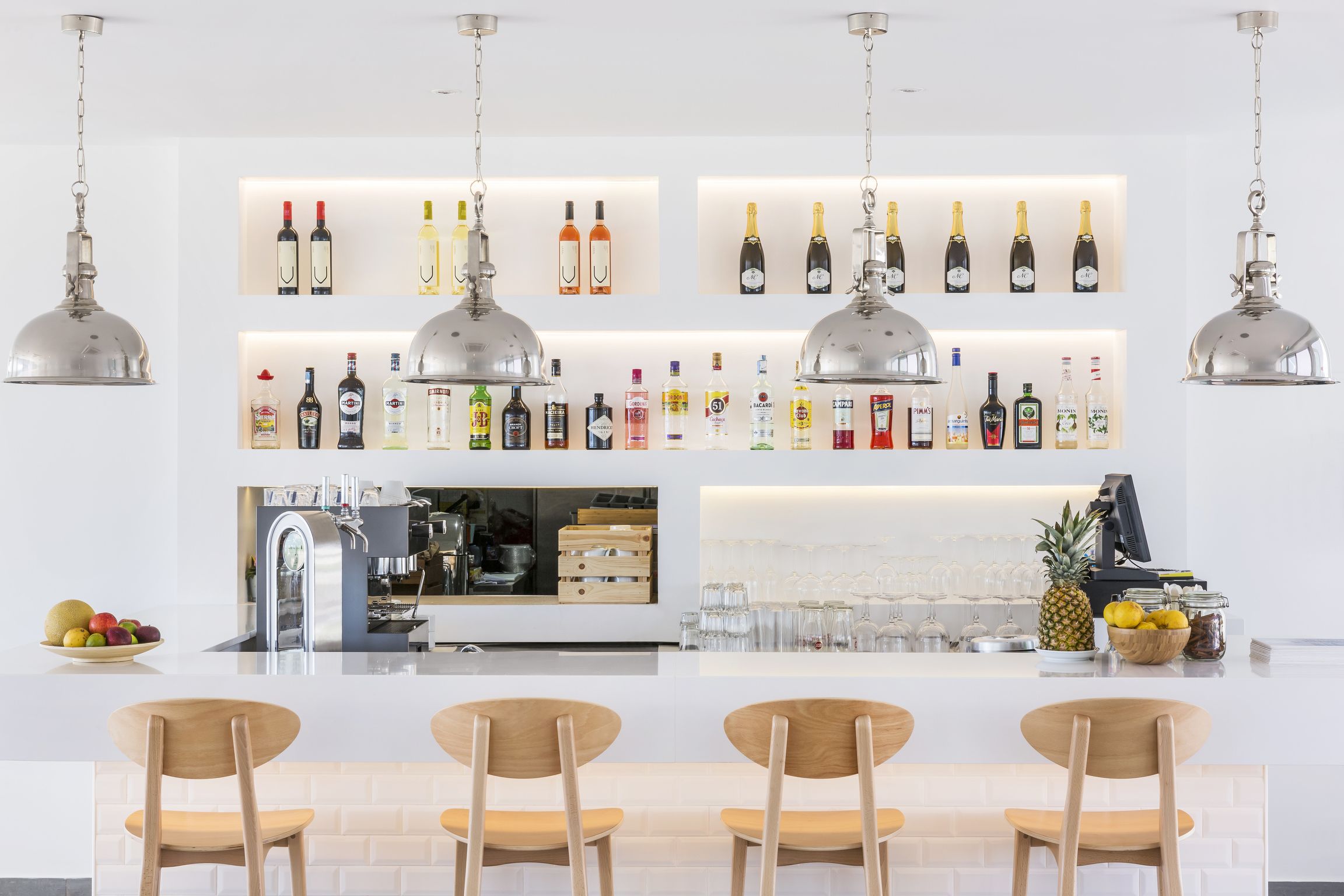 A bar area with multiple shelves of liquor bottles, a kitchen counter, and four wooden chairs.