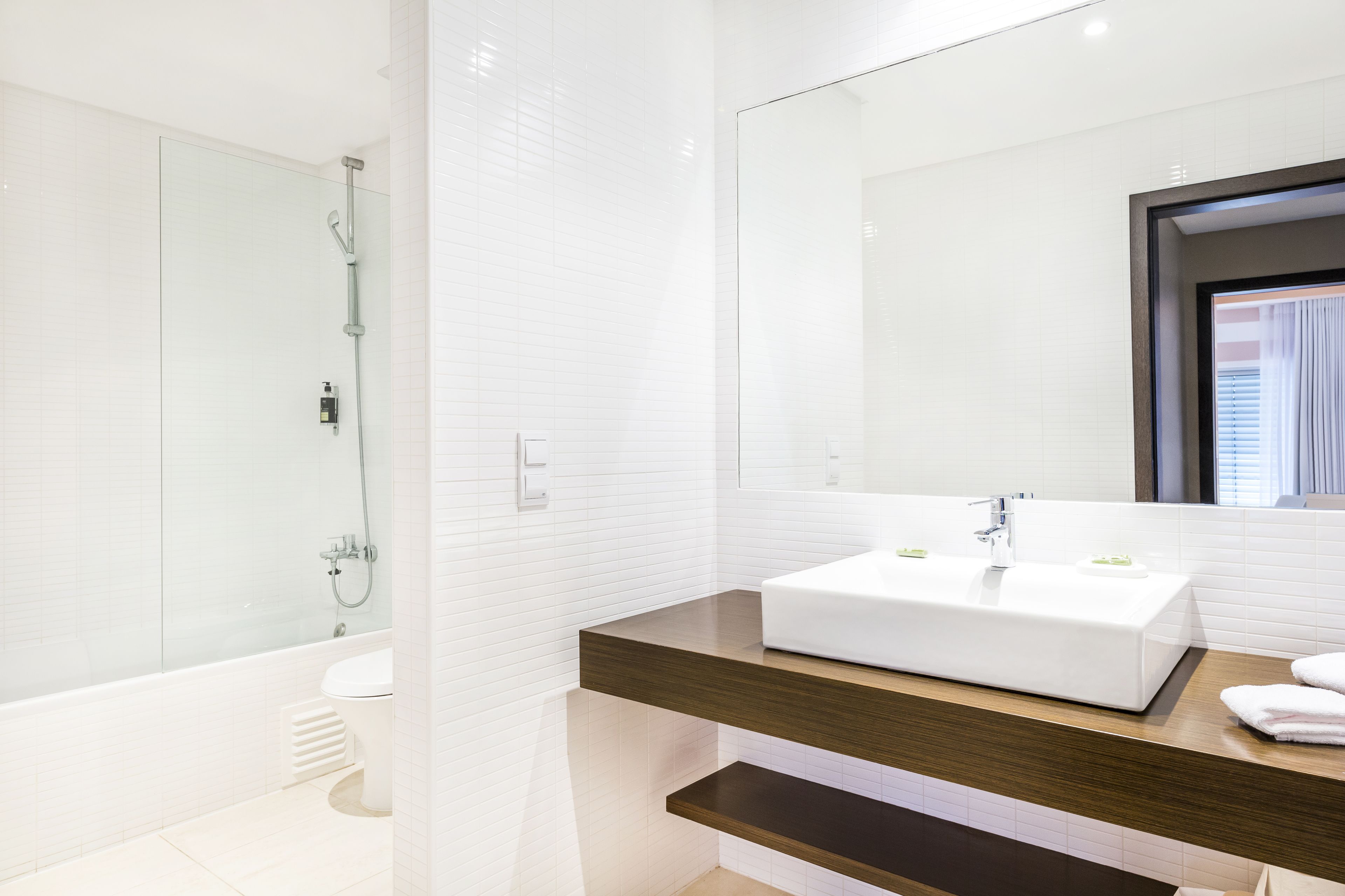 A modern bathroom with a white sink, a glass shower enclosure, and a wooden vanity.