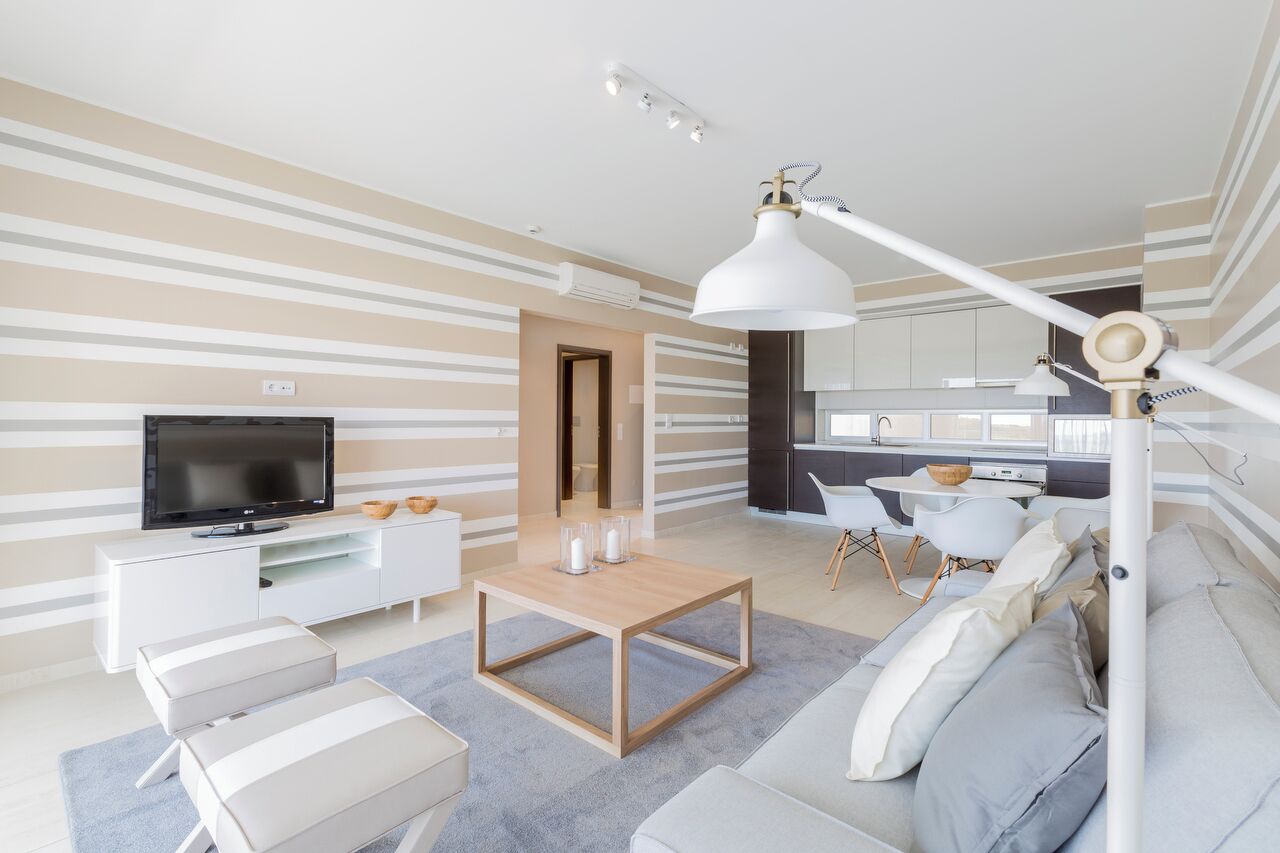 A modern living room with a flat-screen TV, a wooden coffee table, a sofa, and a dining area with a white table and chairs.