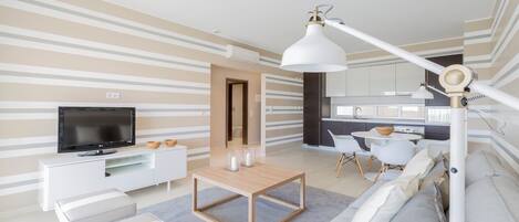 A modern living room with a flat-screen TV, a wooden coffee table, a sofa, and a dining area with a white table and chairs.