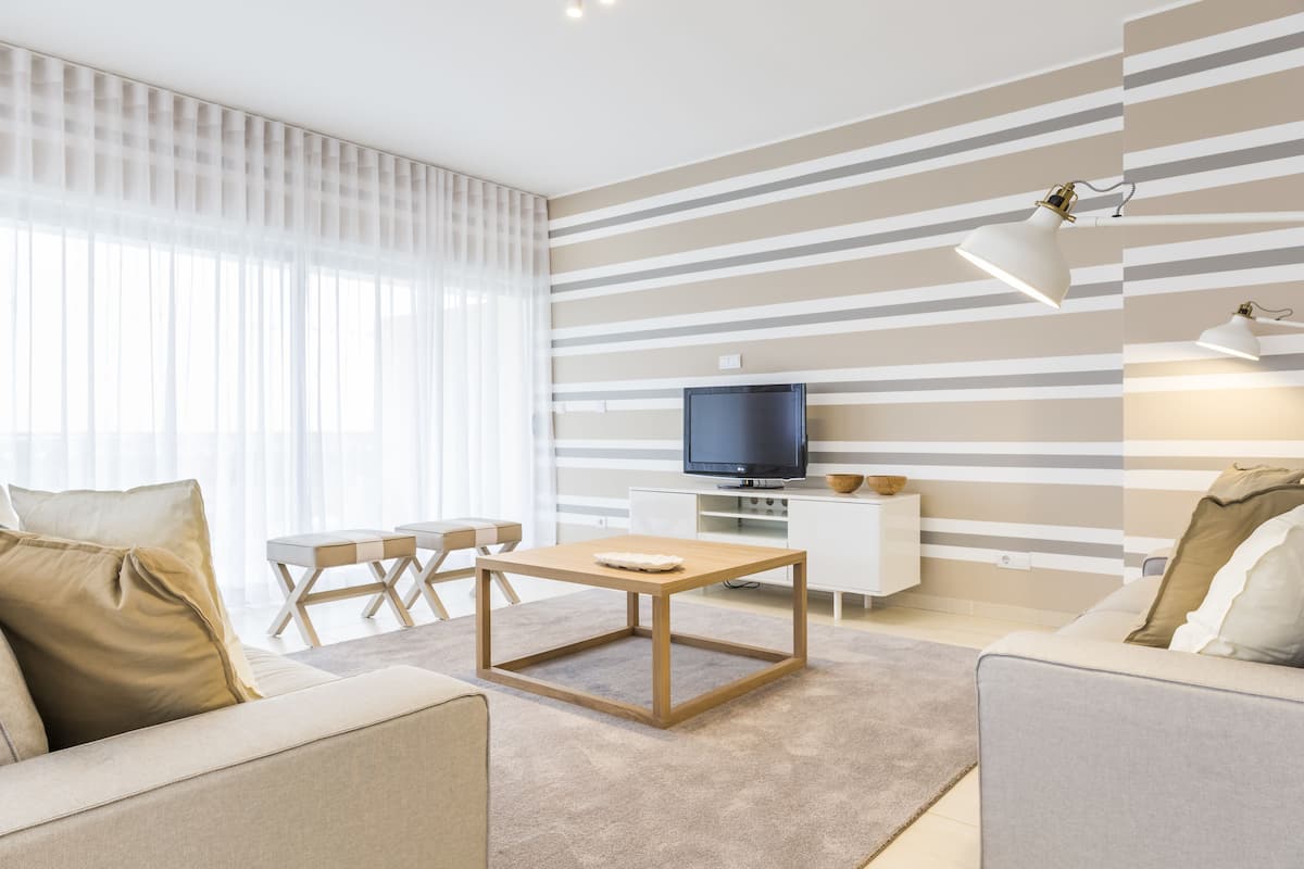 Un salon moderne avec un téléviseur, un canapé, une table basse et un motif rayé sur le mur.