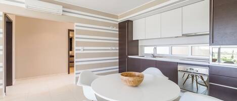 A modern kitchen with white cabinets, a built-in oven, and a dining area with a round table and chairs.