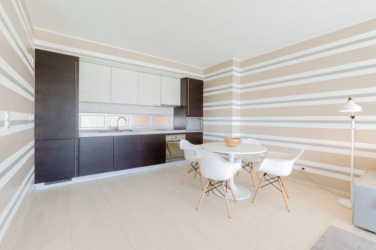 A modern kitchen with dark cabinets, white countertops, and a round dining table with white chairs.