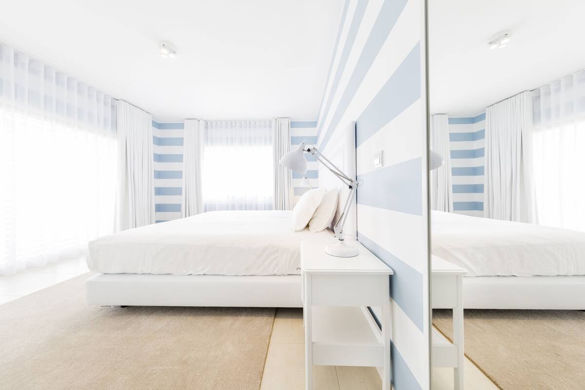 Une chambre d’hôtel moderne avec un grand lit, une table de chevet avec une lampe et un grand miroir.