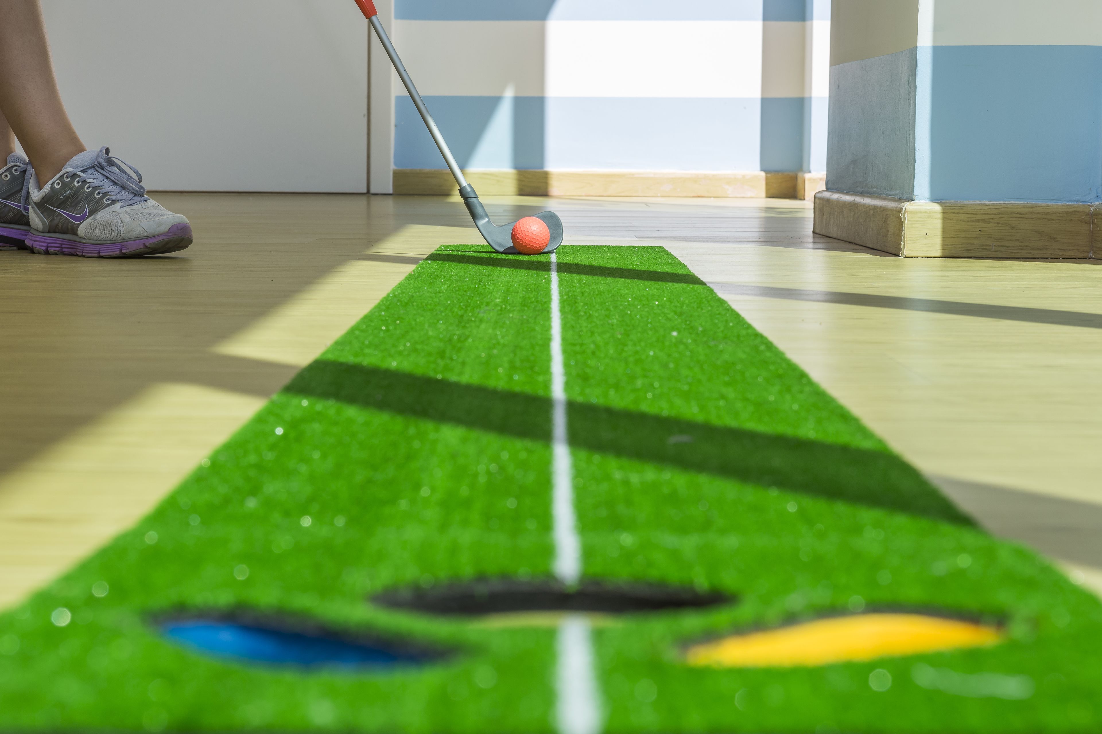 Et grønt træningsunderlag til putting med en golfbold og en putter.