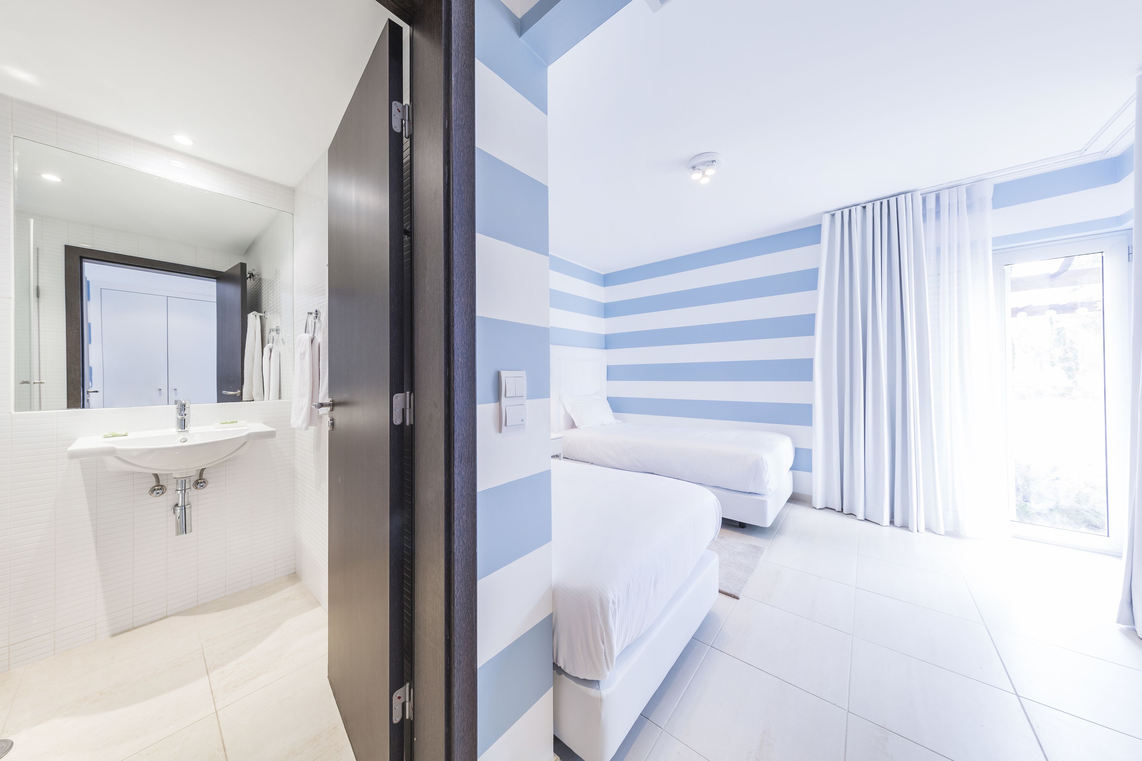 A modern hotel room with a bathroom, a bed, and a large window.
