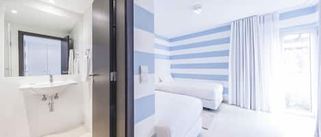 A modern hotel room with a bathroom, a bed, and a large window.