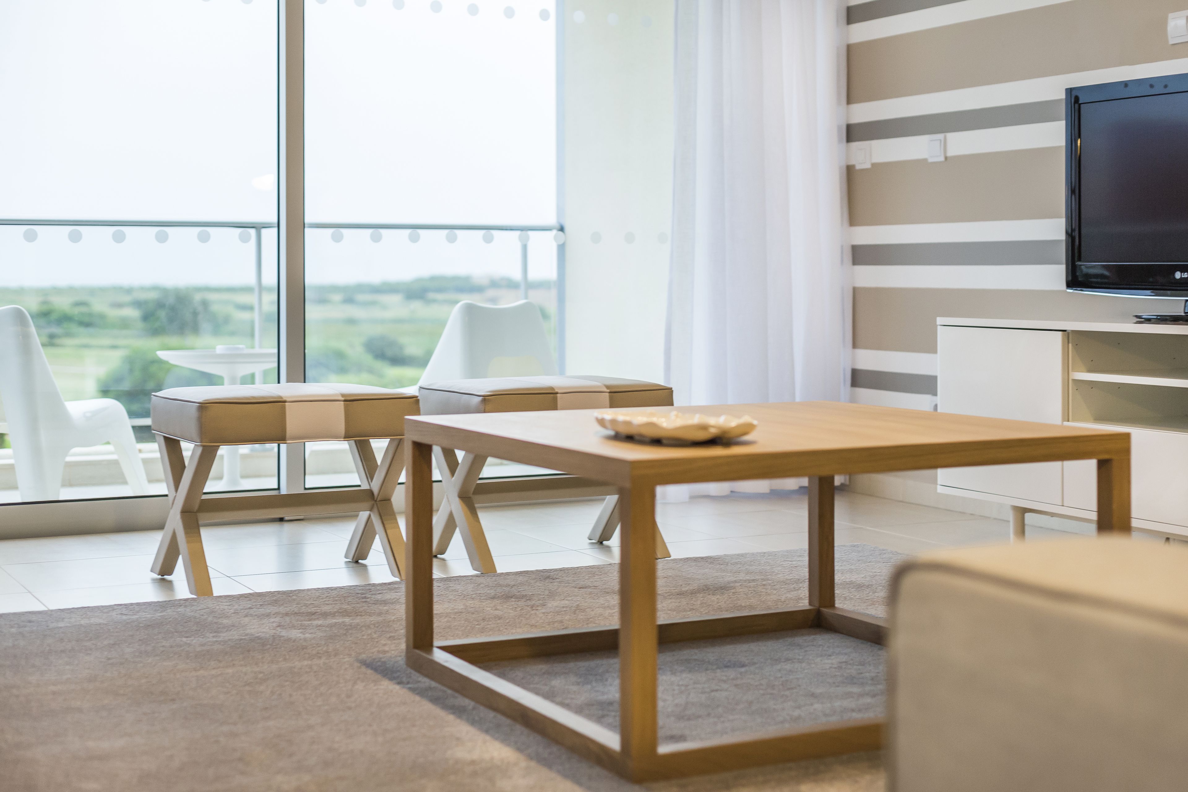 Una sala de estar moderna con una mesa de centro de madera, un televisor y vistas al exterior.