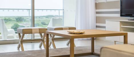 A modern living room with a wooden coffee table, a television, and a view of the outdoors.