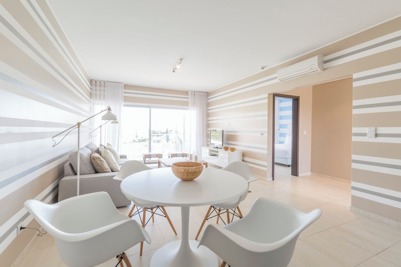 Een moderne woonkamer met een ronde tafel, witte stoelen, een bank en een groot raam.