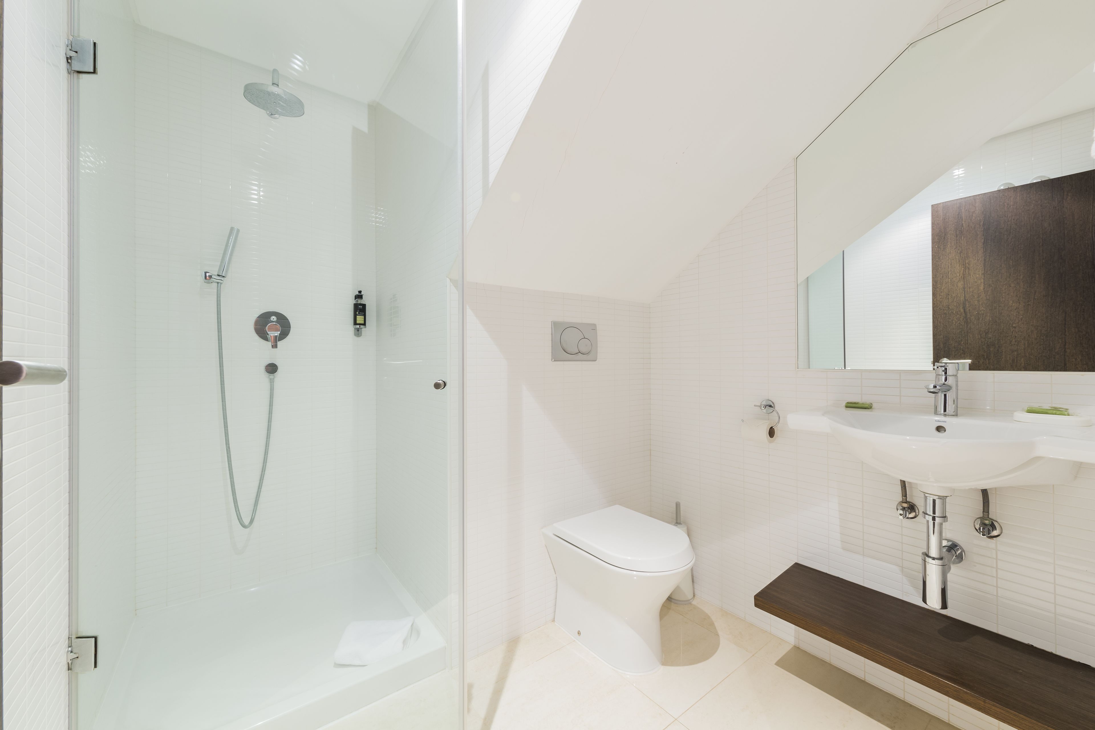 Un baño moderno con ducha de vidrio, inodoro blanco y lavamanos con encimera de madera.