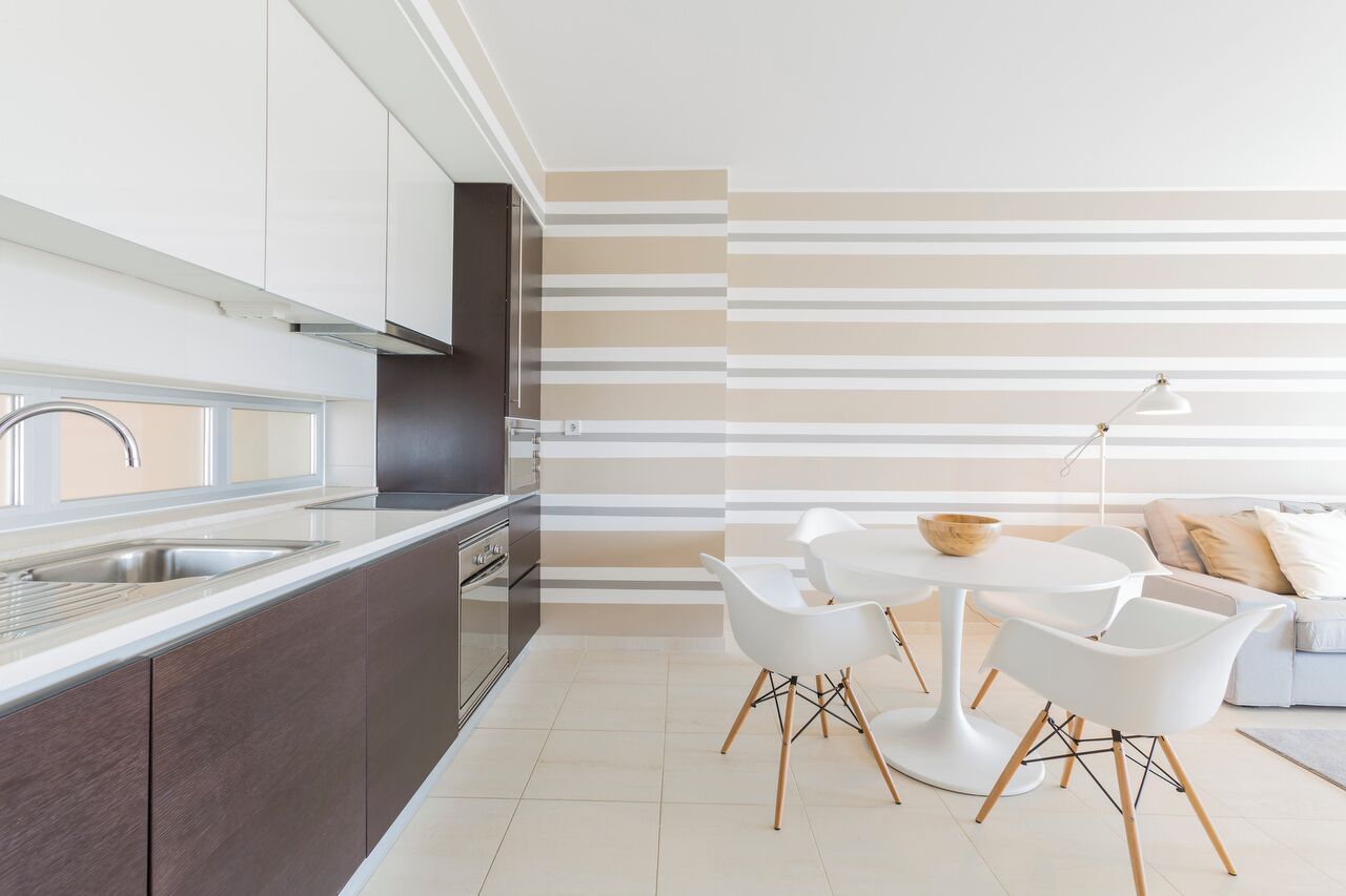A modern kitchen with dark cabinets, a stainless steel sink, and a white dining area with a round table and white chairs.