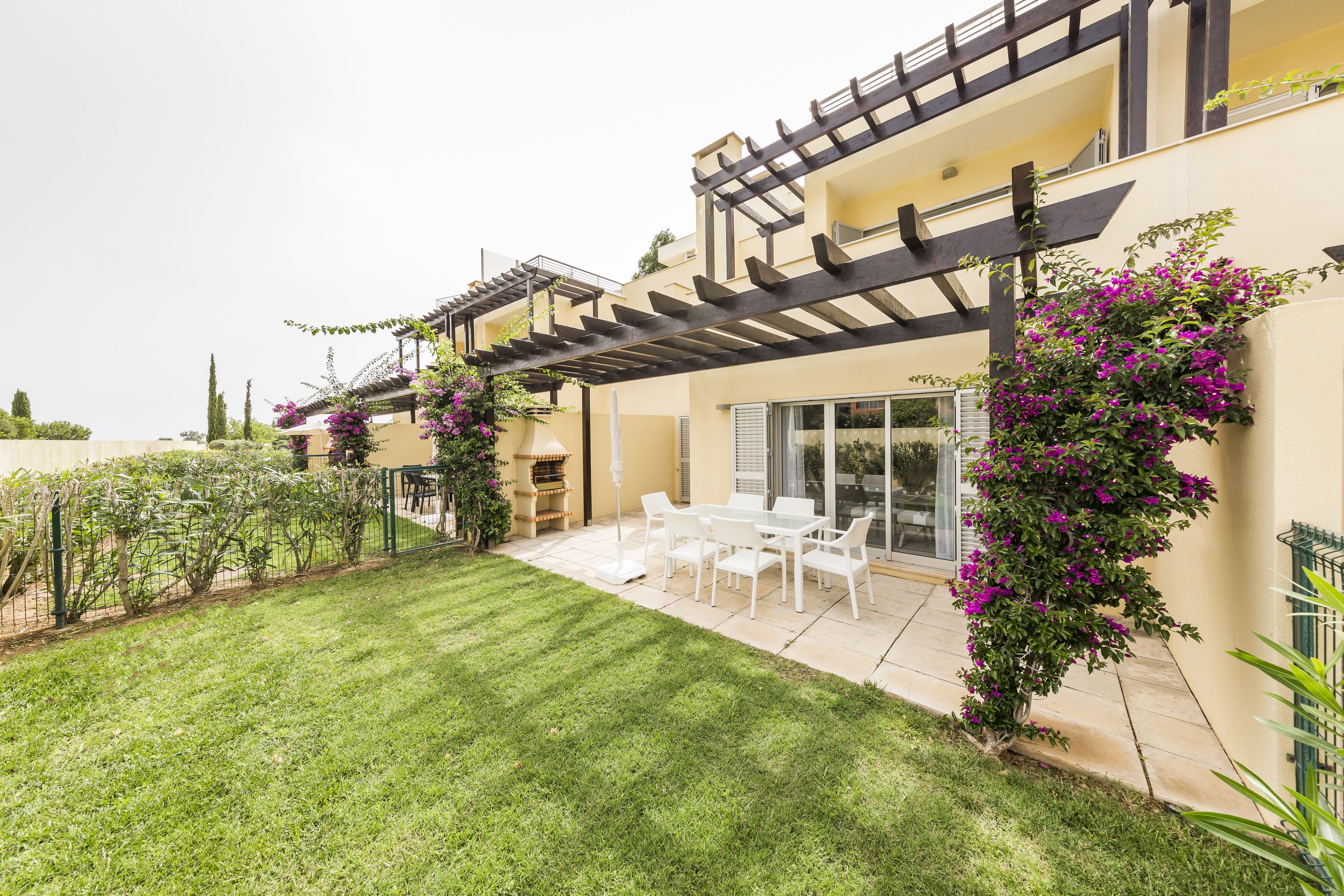 Une maison moderne dotée d’un patio, de meubles blancs et d’un jardin agrémenté de fleurs violettes.