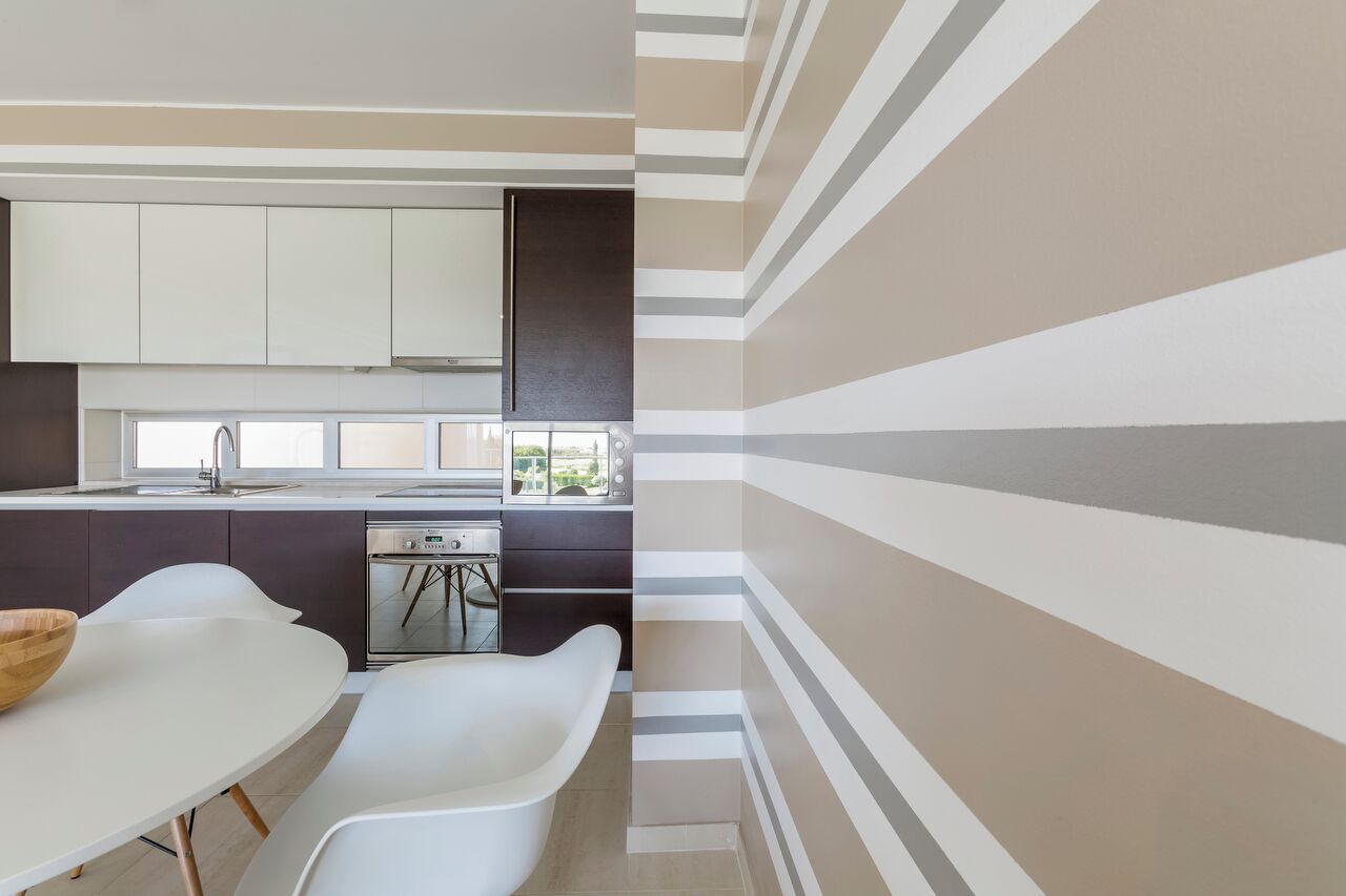 A modern kitchen with white cabinetry, a built-in oven, and a dining area with white chairs.