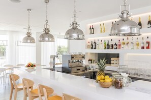 Un espace bar moderne doté d’un comptoir blanc, d’équipements de bar en acier inoxydable et d’une variété de bouteilles et de verres.