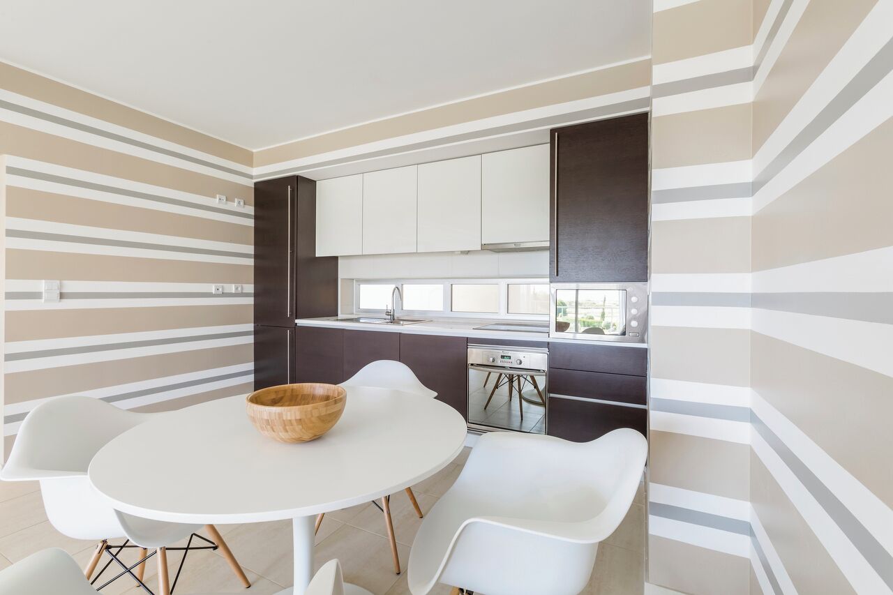 Una cocina moderna con paredes a rayas, armarios blancos y una mesa de comedor redonda con sillas.