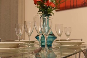 Ein Esstisch mit klarem Glasgeschirr und Tellern, eine Vase mit Blumen und einem dekorativen Wandbild.