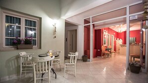 A dining area with a table and chairs, a window with curtains, and a red interior visible through an open door. - Malia Central (Hersonissos)