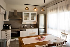 A modern kitchen with white cabinets, a stainless steel refrigerator, and a wooden dining table with chairs.