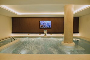 A spa area with a large hot tub, a wooden panel wall, and a television screen. - Dos Reyes Hotel (Mar del Plata)