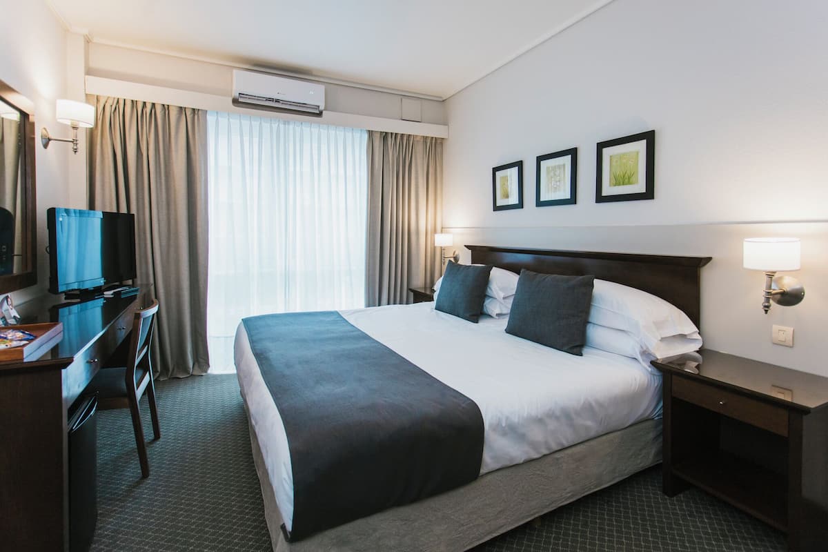 Una habitación de hotel con una cama grande, un escritorio con televisor y una ventana con cortinas.