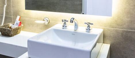 A bathroom with a white sink, a mirror, and a hairdryer on the wall.