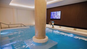An indoor swimming pool with a large column, a television on the wall, and a wooden panel design. - Dos Reyes Hotel (Mar del Plata)
