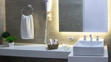 A modern bathroom with a large mirror, a towel rack, a hairdryer, and a sink with two faucets.
