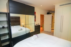 Ein Hotelzimmer mit Bett, Kleiderschrank, Schminktisch und einem Spiegel, der den Raum wiedergibt.