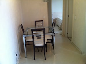 Un coin repas avec une table à plateau en verre et quatre chaises, un plancher de couleur claire et un mur sobre.