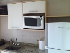 Une cuisine équipée d’un four à micro-ondes posé sur une étagère, d’un évier et d’un réfrigérateur.