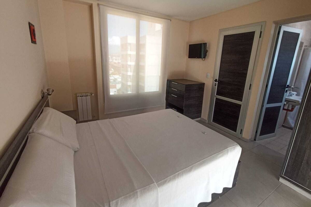 Un dormitorio con cama, cómoda, televisor y puerta corredera al baño.