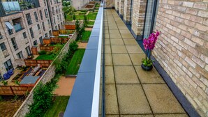 Uma varanda estreita com vista para um pátio, edifícios de tijolo e um vaso de planta.