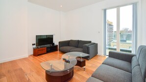 Uma sala de estar moderna com uma televisão de tela plana, um sofá cinza e uma mesa de centro de vidro.