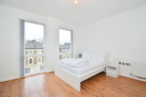 Une chambre à coucher moderne avec un grand lit, une table de chevet et une fenêtre donnant sur des immeubles.