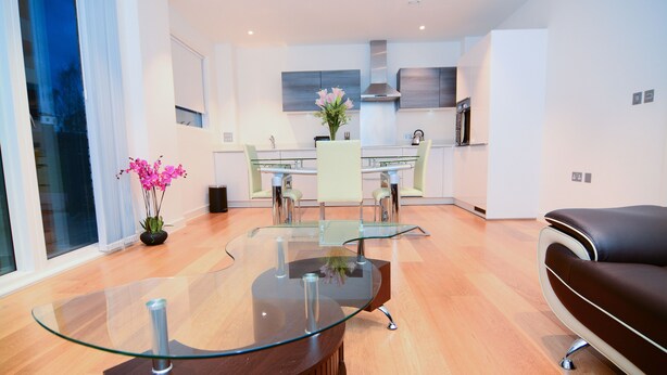 Uma sala de estar moderna com uma mesa de centro de vidro, um sofá de couro e uma área de jantar com mesa e cadeiras de vidro.