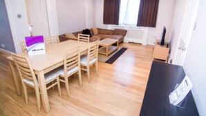 Una sala de estar moderna con una mesa de comedor de madera y sillas, un sofá marrón y un mueble bajo para televisión negro.