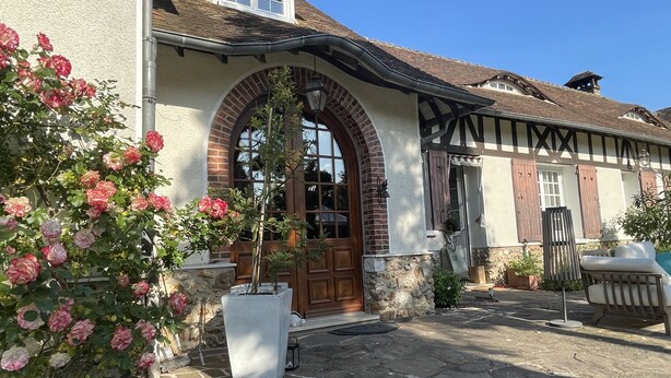 A traditional building with a stone facade, a large arched entrance, and a potted plant with pink flowers. - La Collinière (Sainte-Gemme-Moronval)