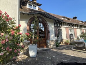 A traditional building with a stone facade, a large arched entrance, and a potted plant with pink flowers. - La Collinière (Sainte-Gemme-Moronval)