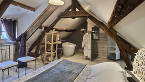 A cozy attic bedroom with a sloped ceiling, a large bed, a wooden ladder, a bathtub, and a small table. - La Collinière (Sainte-Gemme-Moronval)